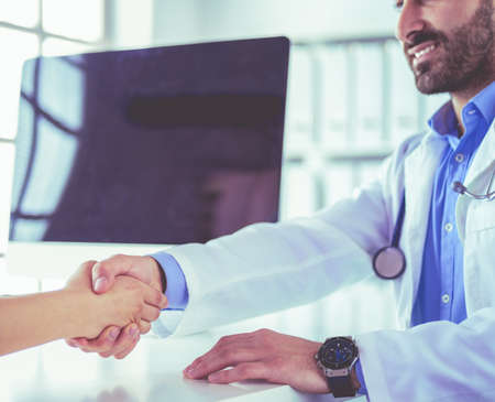 Doctor shaking hands to patient in the office at deskの写真素材