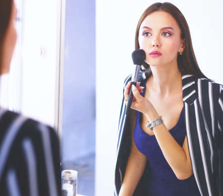 Beauty woman applying makeup. Beautiful girl looking in the mirror and applying cosmetic with a big brushの写真素材
