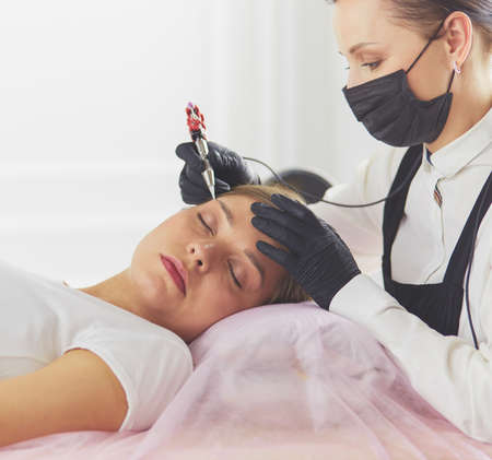 Young woman undergoing procedure of eyebrow permanent makeup in beauty salonの写真素材