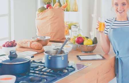 Attractive woman holding a glass of orange juice while standing in the kitchenの写真素材