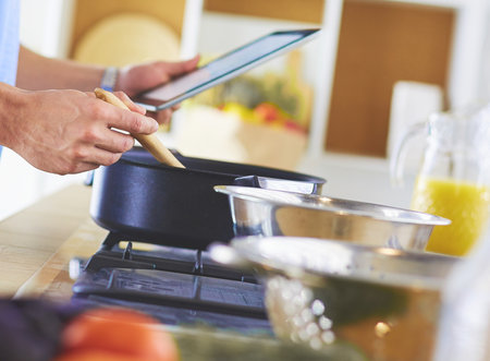 Man following recipe on digital tablet and cooking tasty and healthy food in kitchen at homeの写真素材