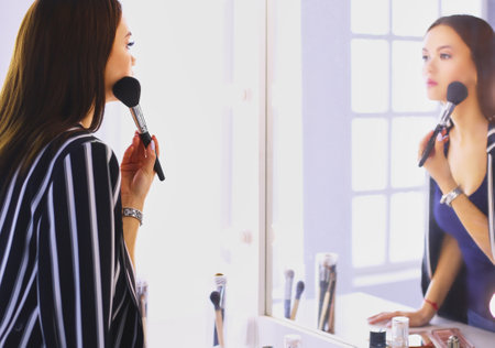 Beauty woman applying makeup. Beautiful girl looking in the mirror and applying cosmetic with a big brushの写真素材