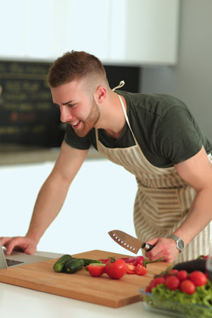 Portrait of man cooking vegetable in the kitchen while looking at a laptop computer on the tableの写真素材