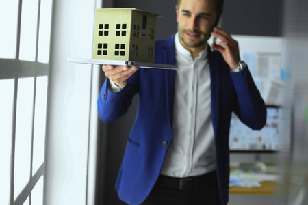 Businessman holding house miniature on hand standing in office.の写真素材