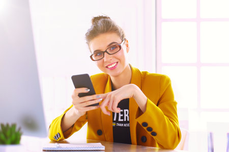 Businesswoman sitting in office with laptop on telephoneの写真素材