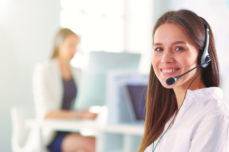 Smiling businesswoman or helpline operator with headset and computer at officeの写真素材