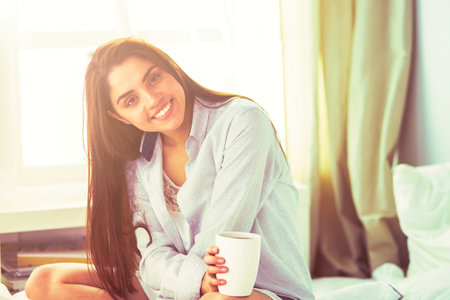 Woman sitting in bed reading a book and having breakfastの写真素材