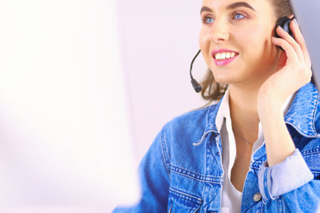 Happy charming young woman sitting and working with laptop using headset in officeの写真素材