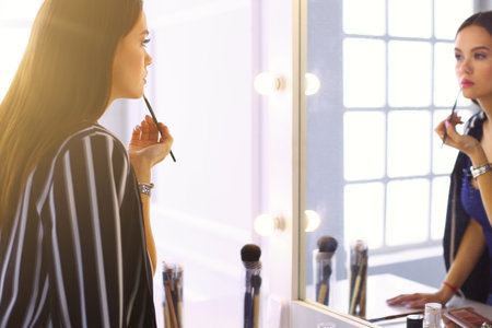 Young woman applying lipstick in front of a mirrorの写真素材