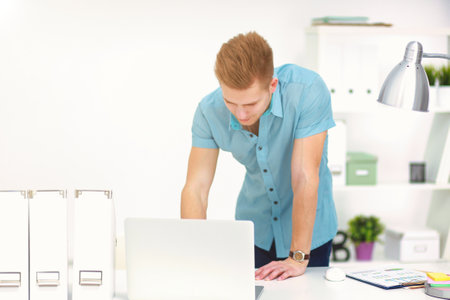 Businessman standing at table working with laptop computer, leaning on deskの写真素材