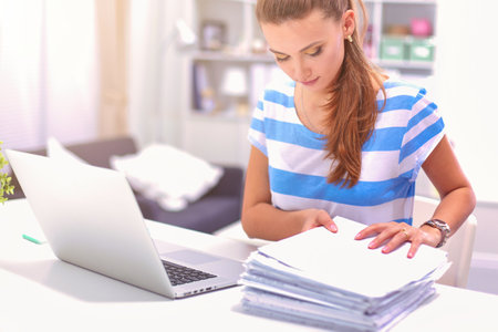 Smiling woman with documents sitting on the desk with laptop.の写真素材