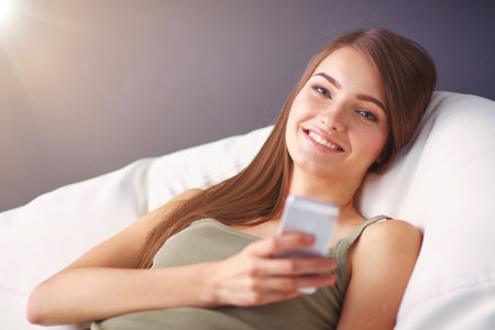Pretty woman in her living room lying on the couch sending messの写真素材