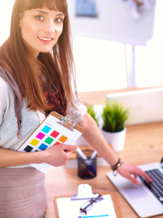 Young attractive fashion designer standing by desk in office, holding foldersの写真素材