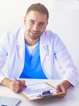Portrait of a male doctor with laptop sitting at desk in medical office.の写真素材