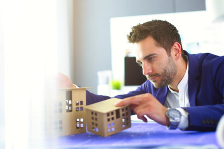 Businessman holding house miniature on hand standing in office.の写真素材