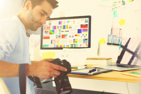 Portrait of young designer sitting at graphic studio in front of laptop and computer while working online.の写真素材
