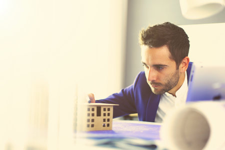 Businessman holding house miniature on hand standing in office.の写真素材