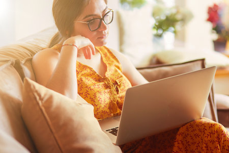 Young woman sitting on couch working on laptop computer at homeの写真素材