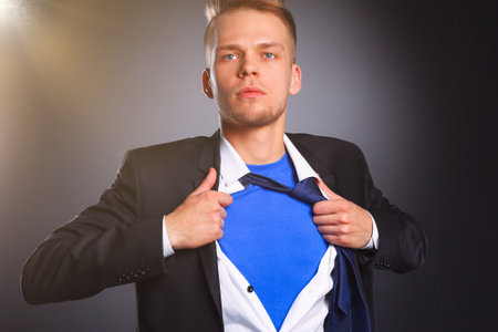 Young businessman acting like a super hero and tearing his shirt, isolated on gray backgroundの写真素材