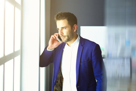 Business man in suit talking on phone and looking away near the window.の写真素材