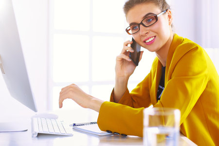 Businesswoman concentrating on work, using computer and cellphone in officeの写真素材