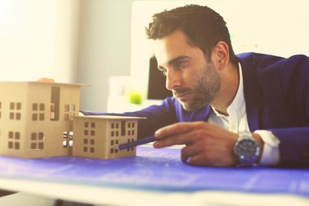 Businessman holding house miniature on hand standing in office.の写真素材