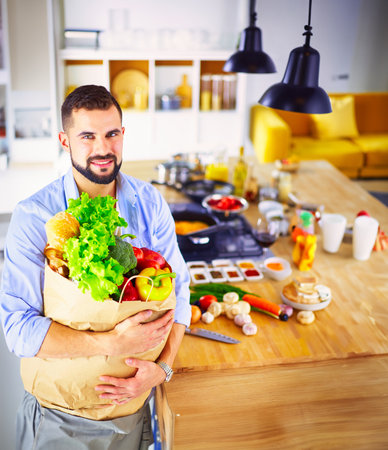 Man holding paper bag full of groceries on the kitchen background. Shopping and healthy food conceptの写真素材