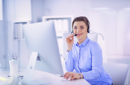Serious pretty young woman working as support phone operator with headset in officeの写真素材