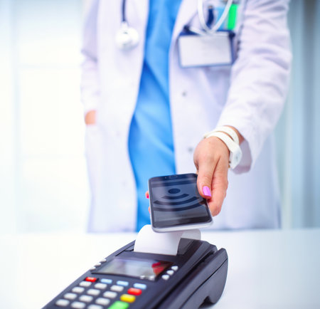 Doctor is holding payment terminal in hands. Paying for health care. Doctorの写真素材