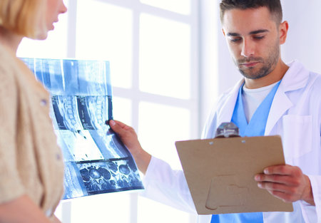 Handsome doctor is talking with young female patient and making notes while sitting in his office.の写真素材