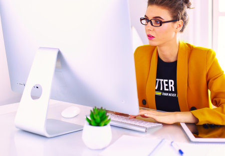 Young confident businesswoman working at office desk and typing with a laptopの写真素材