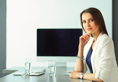 Back view of smiling business woman sitting by the table with laptop and looking at camera in officeの写真素材
