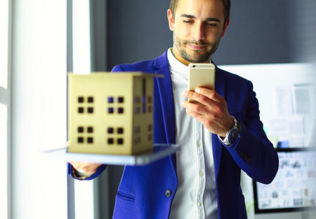 Businessman holding house miniature on hand standing in office.の写真素材