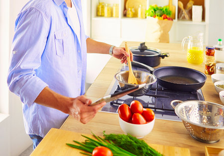 Man following recipe on digital tablet and cooking tasty and healthy food in kitchen at homeの写真素材