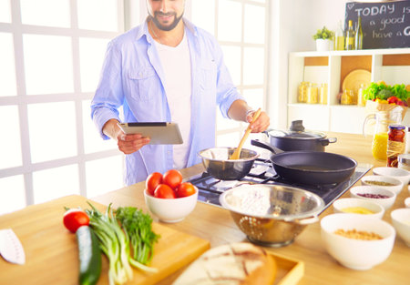 Man following recipe on digital tablet and cooking tasty and healthy food in kitchen at homeの写真素材