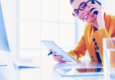 Portrait of beautiful woman making call while sitting at her workplace in front of laptop and working on new projectの写真素材