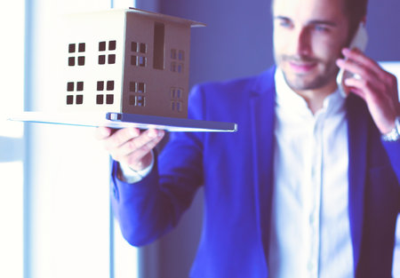 Businessman holding house miniature on hand standing in office.の写真素材