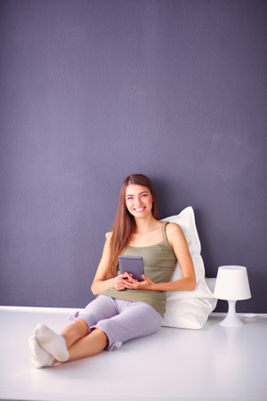 Pretty brunette woman sitting on the floor with a pillow and plane tableの写真素材
