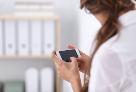 Businesswoman sending message with smartphone in officeの写真素材