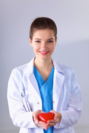 Young woman doctor holding a red heart, standing on grayの写真素材