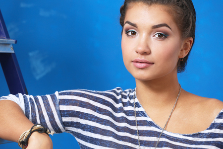 Beautiful young woman doing wall painting, standing near ladderの写真素材