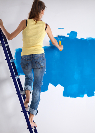 Beautiful young woman doing wall painting, standing near ladderの写真素材