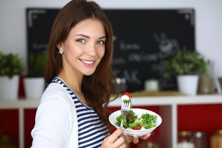 Young woman eating salad and holding a mixed salad .