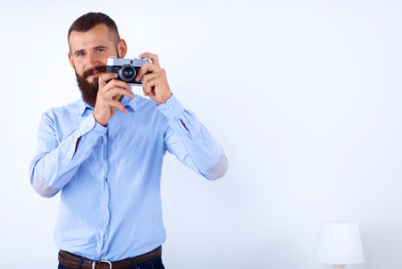 Young beard man holding a camera while standing against white background.の写真素材