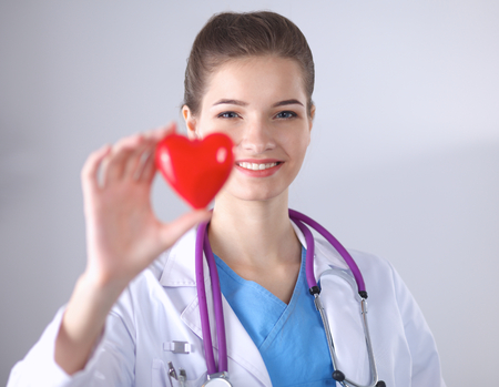 Young woman doctor holding a red heart, standing on grayの写真素材