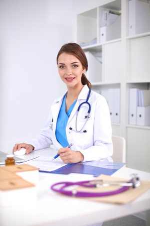 Beautiful young smiling female doctor sitting at the deskの写真素材