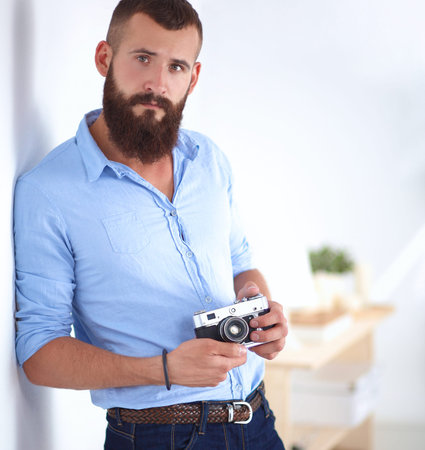 Young beard man holding a camera while standing against white background.の写真素材