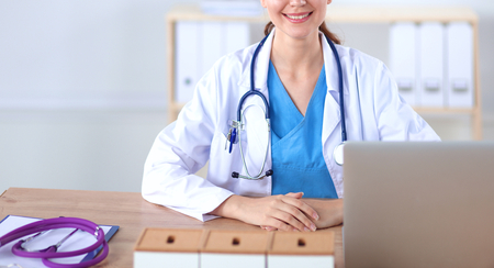 Beautiful young smiling female doctor sitting at the deskの写真素材