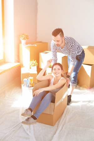 Happy couple having fun and riding in cardboard boxes at new home.の写真素材