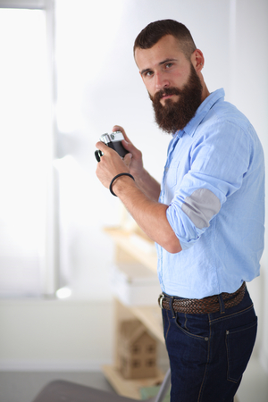 Young beard man holding a camera while standing against white background.の写真素材